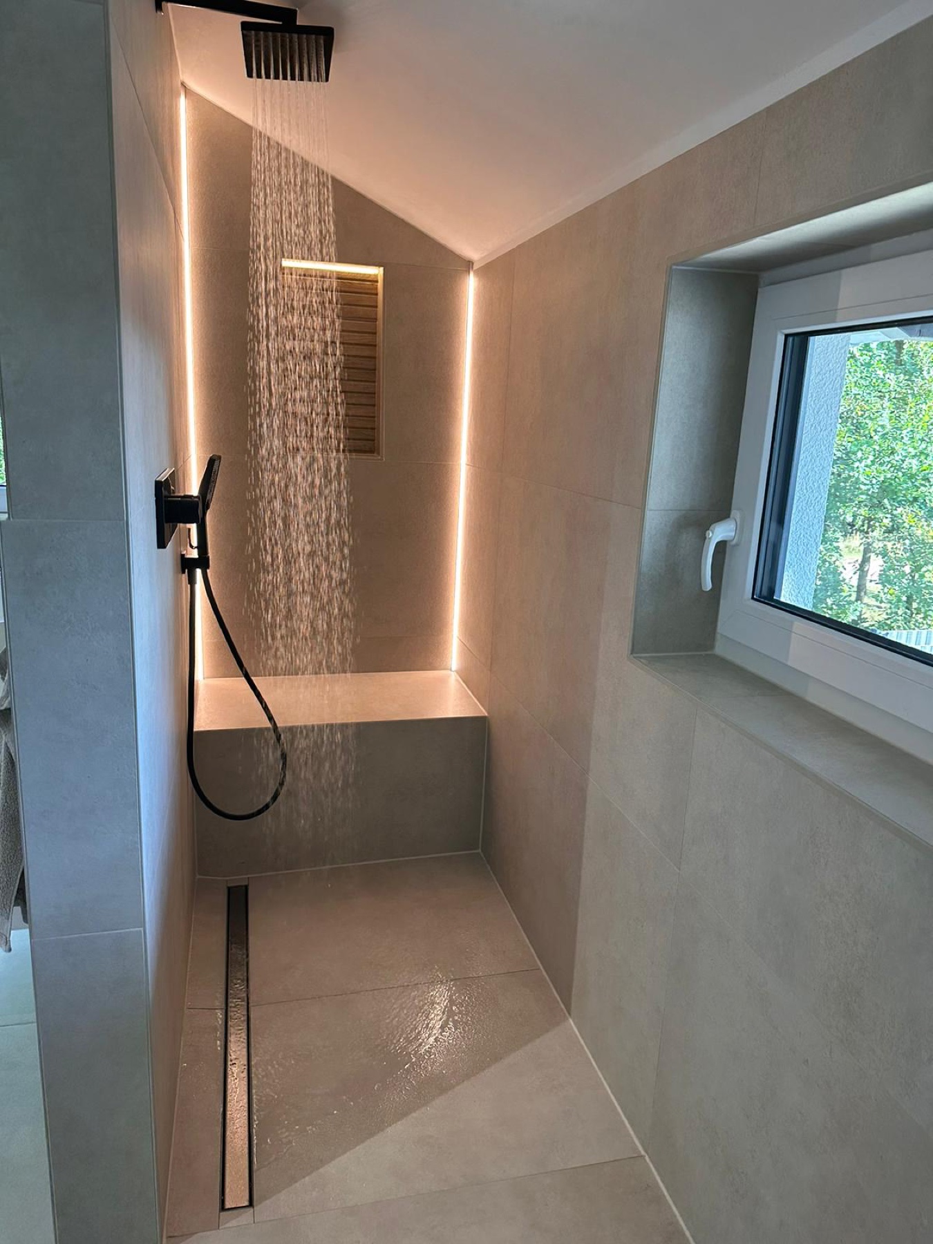 Dusche mit grauen Fliesen und indirekt beleuchteter Wandkante